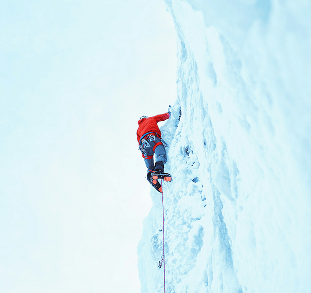 Mann mit roter Jacke beim Eisklettern am Seil an einer Eiswand