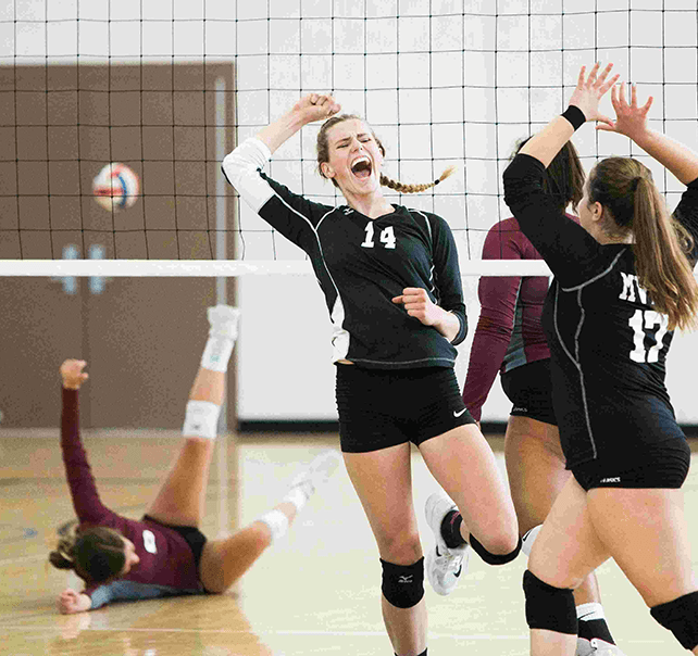 Fünf Frauen in schwarzen Trikots am Volleyball spielen in einer Turnhalle